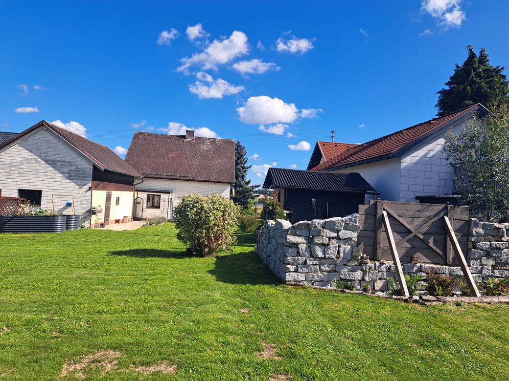 Natursteinmauer mit Blick auf Haus und Nebengebäude